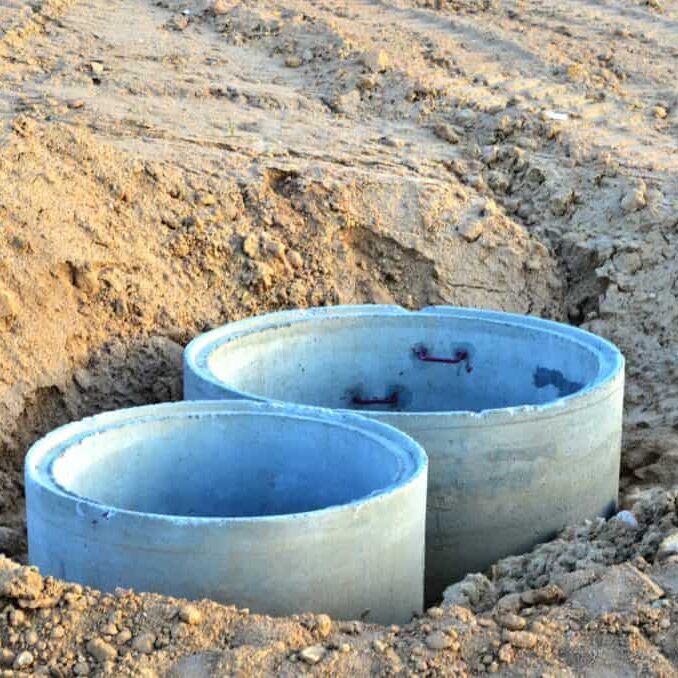 Installation of concrete sewer wells in the ground at the construction site. The use of reinforced concrete rings for cesspools, overflow septic tanks. Improvement of wells and storm sewage - Image